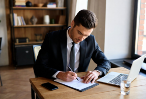 Un homme signe un contrat, devant son ordinateur.