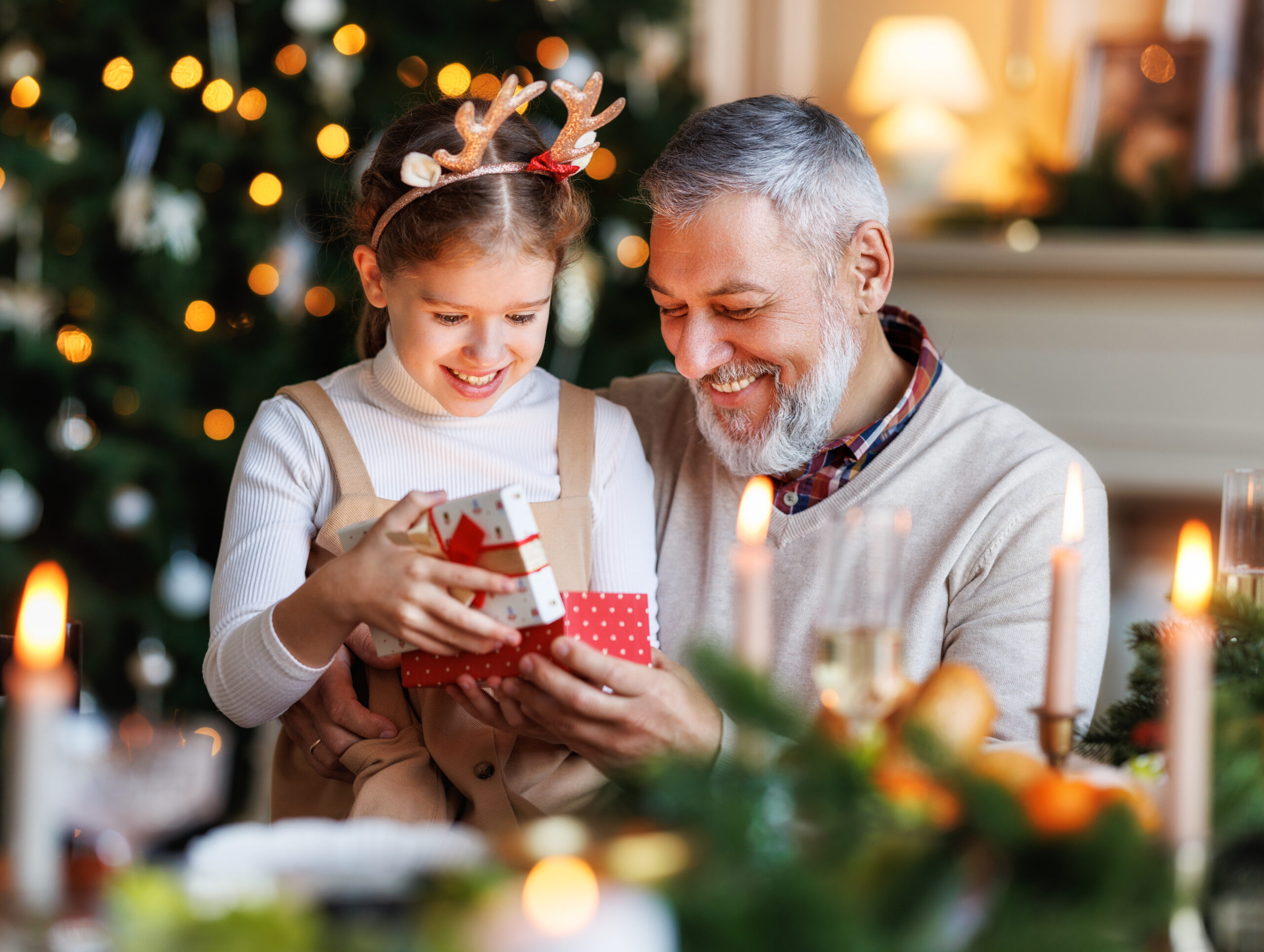 Un grand-père heureux offrant un cadeau à sa petite-fille : un contrat d'assurance vie au pied du sapin. Ils sont assis à la table à manger près de l’arbre de Noël décoré à la maison