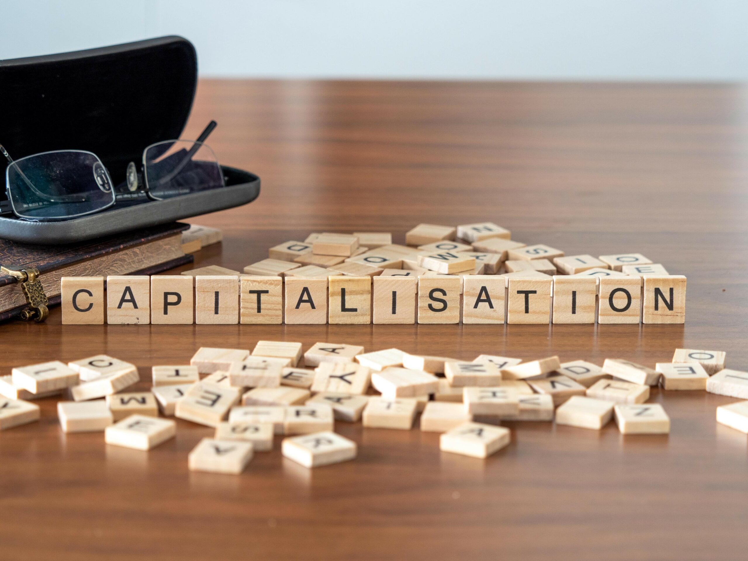 Carrés en bois alignés sur une table pour former le mot "Capitalisation" en noir, à la manière d'un jeu de scrabble.