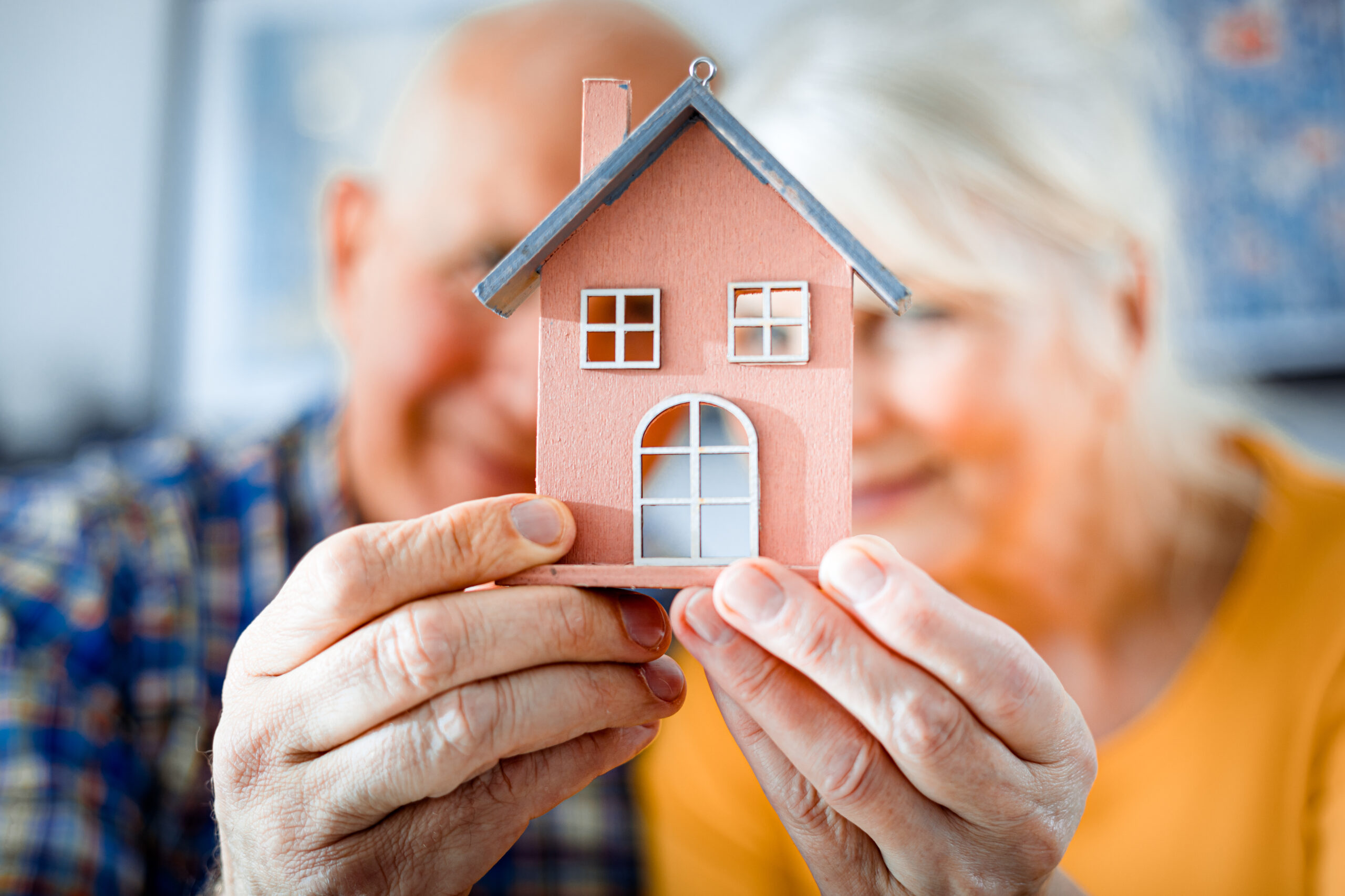 Un couple de personnes âgées tenant une maquette de maison