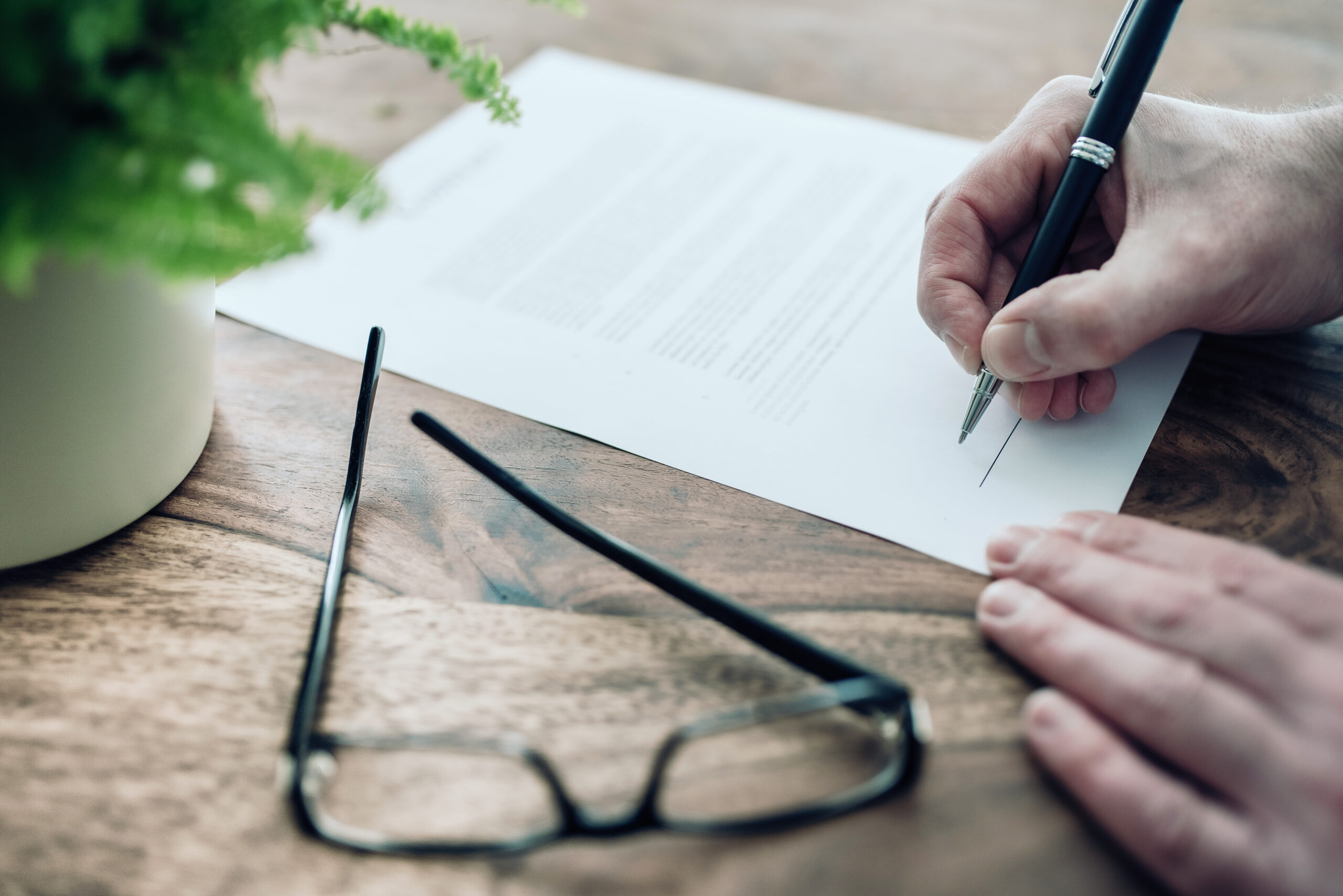 Gros plan d'un homme d'affaires signant sa clause bénéficiaire sur une table rustique en bois.